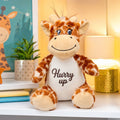 A soft plush giraffe toy sitting on a cozy bed, featuring detailed custom embroidery on its belly in a modern child's bedroom.
