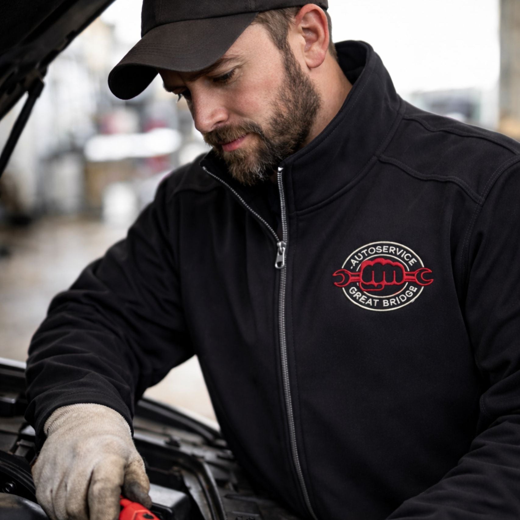Man wearing a branded workwear softshell jacket with embroidered logo while repairing a car in a workshop