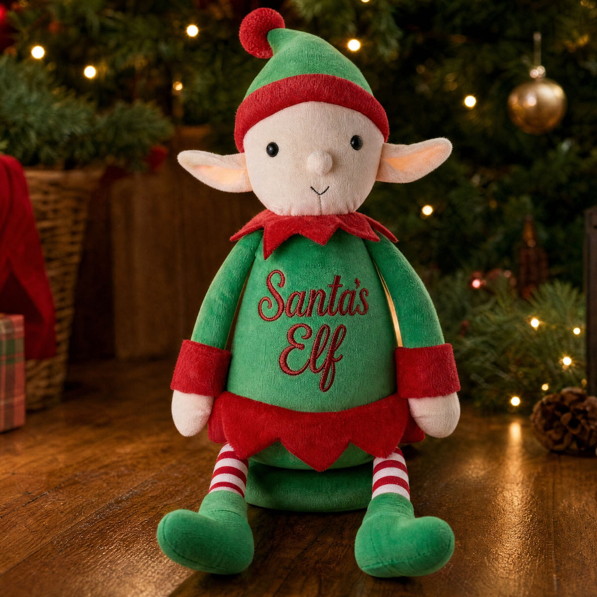 Personalised Christmas elf Jolly sitting on the floor beside a Christmas tree