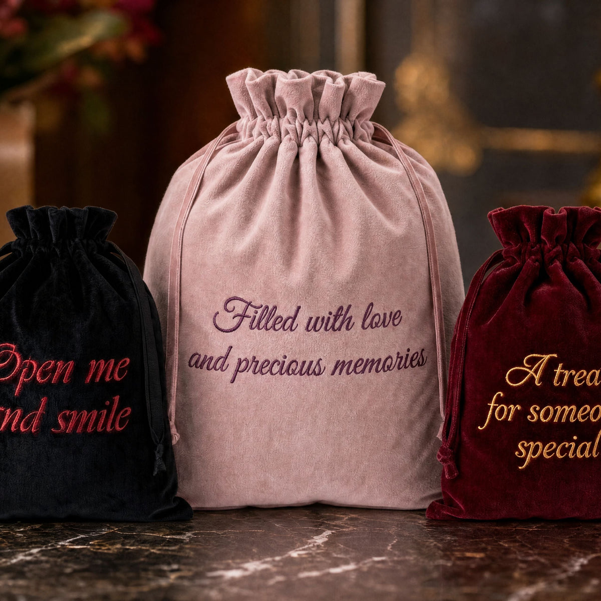 Three personalised velvet drawstring gift bags in black, ruby red and Rose Quartz pink, each featuring custom embroidery